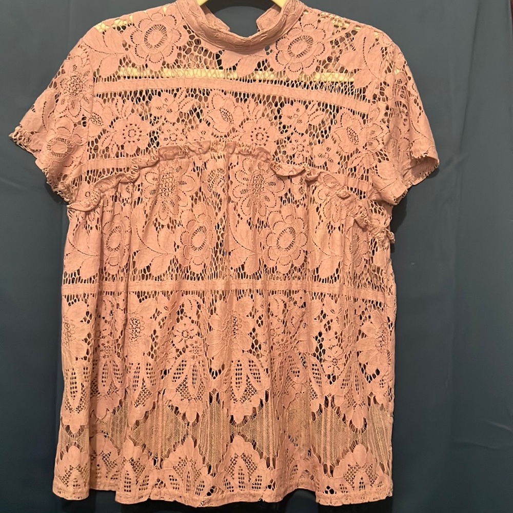 A light pink over shirt with floral patter holes in it.